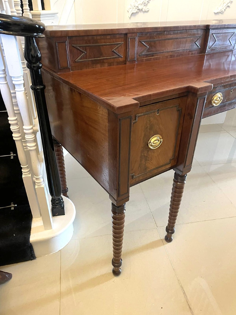 A large George III figured mahogany sideboard featuring a raised gallery, central drawers with brass handles, side cupboards, and turned reeded legs. View VII