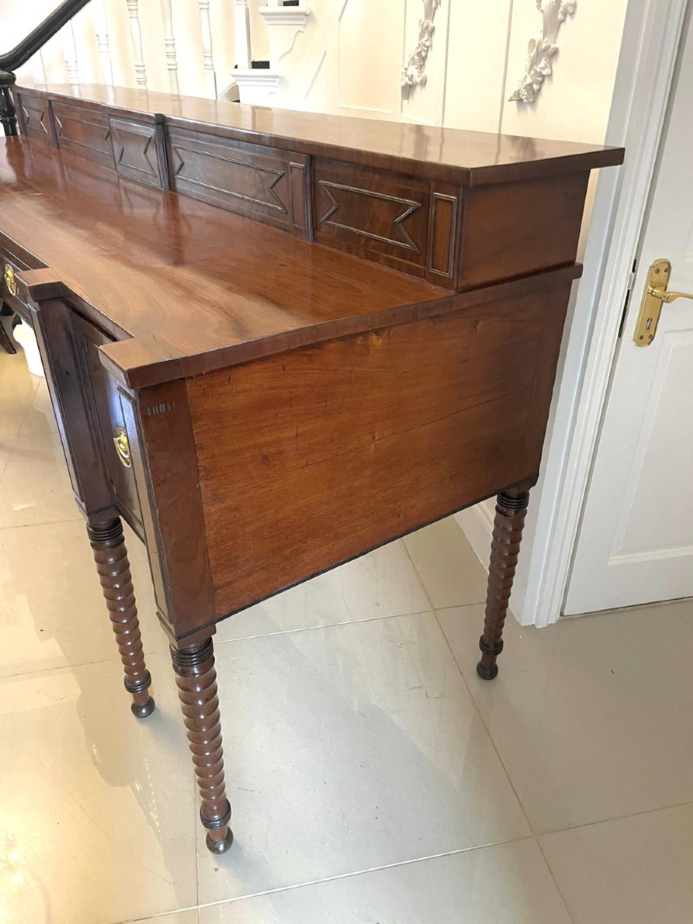 A large George III figured mahogany sideboard featuring a raised gallery, central drawers with brass handles, side cupboards, and turned reeded legs. View VIII