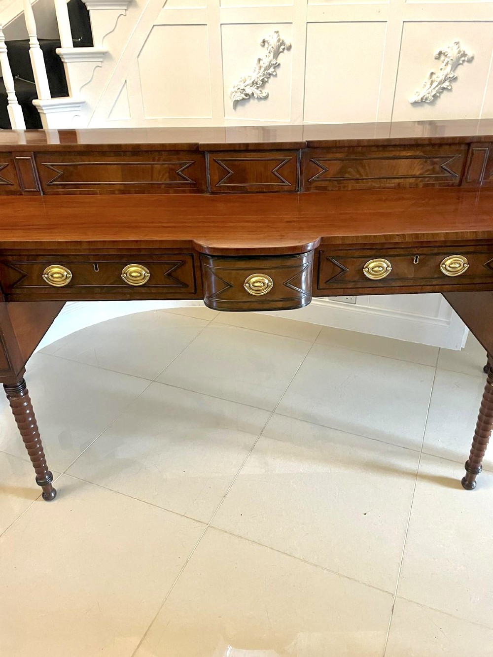 A large George III figured mahogany sideboard featuring a raised gallery, central drawers with brass handles, side cupboards, and turned reeded legs. View XI