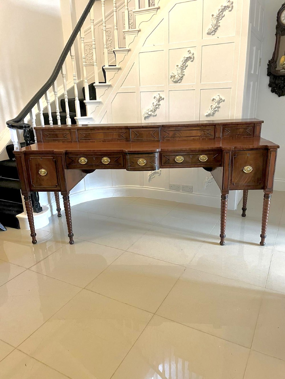 A large George III figured mahogany sideboard featuring a raised gallery, central drawers with brass handles, side cupboards, and turned reeded legs. View XIII