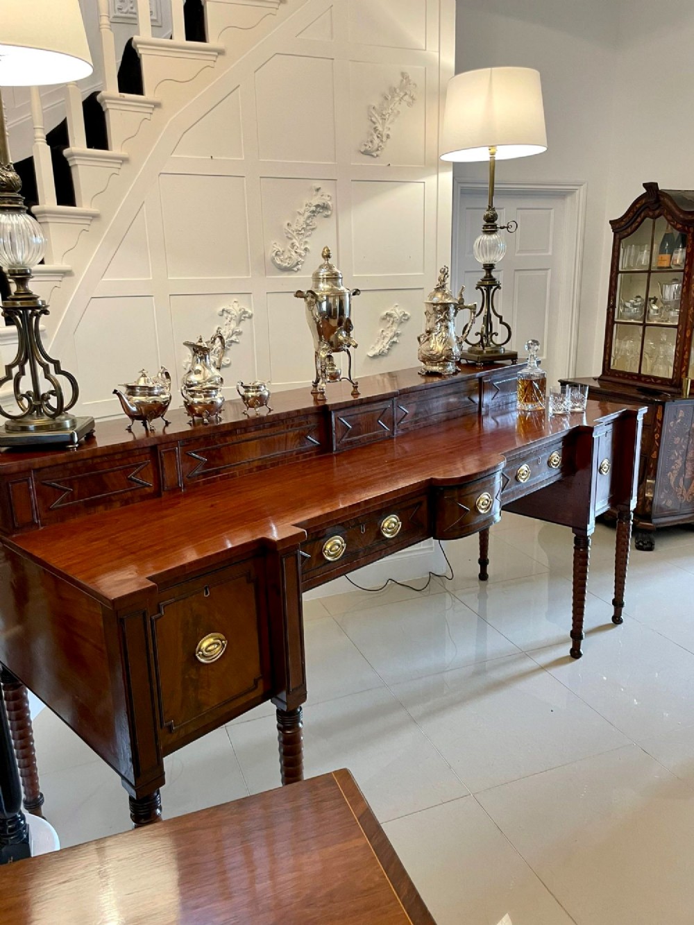 A large George III figured mahogany sideboard featuring a raised gallery, central drawers with brass handles, side cupboards, and turned reeded legs. View XIV