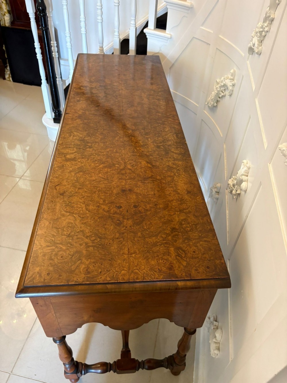 An antique Edwardian burr walnut dresser base featuring three drawers, brass drop handles, a scalloped apron, and turned legs connected by stretchers. View VIII