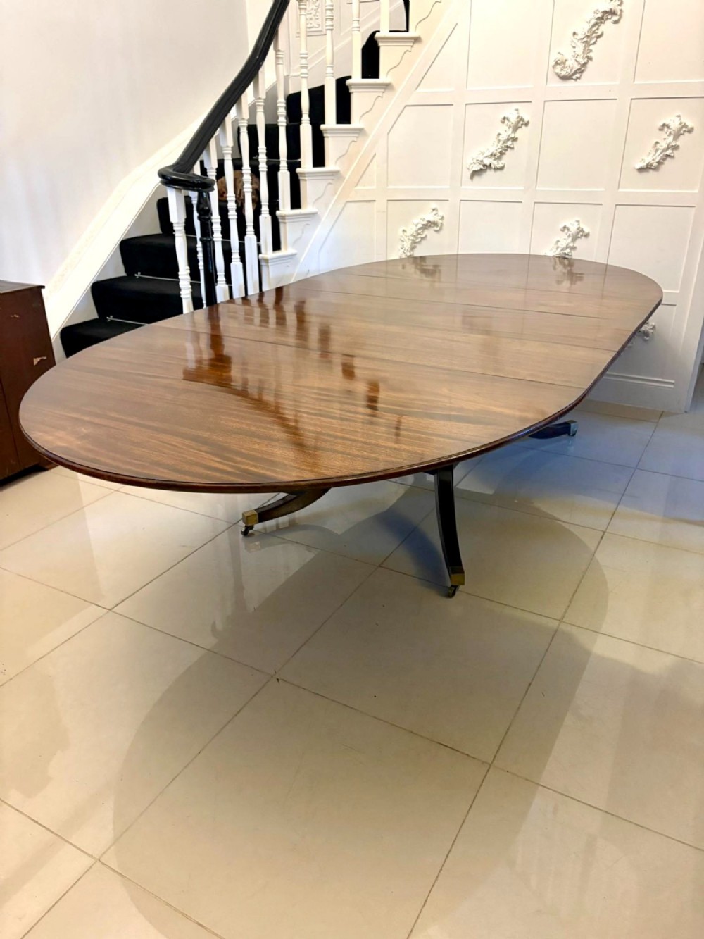 An antique oval extending mahogany dining table on splayed pedestal legs with brass castors. View VII