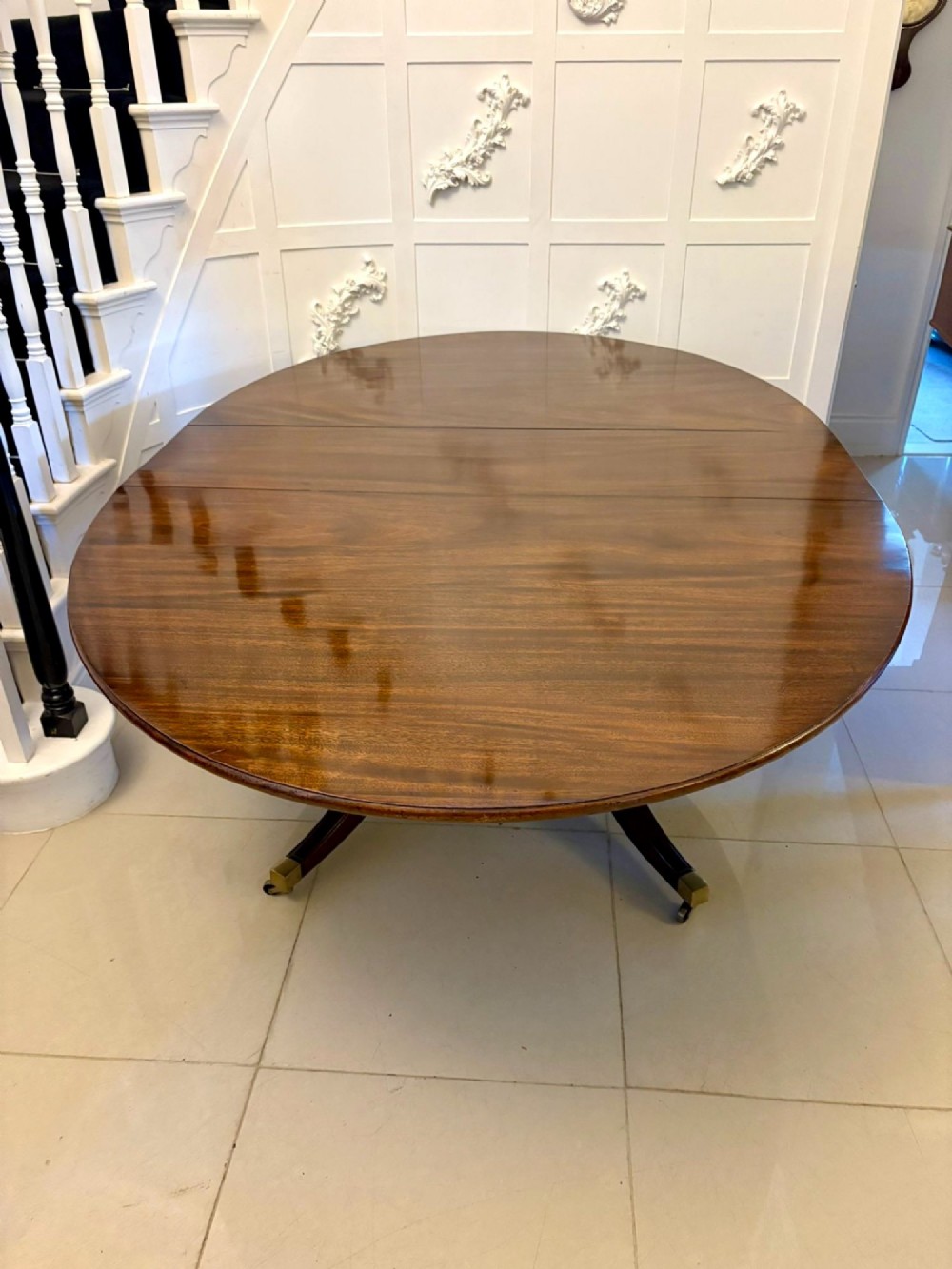 An antique oval extending mahogany dining table on splayed pedestal legs with brass castors.
