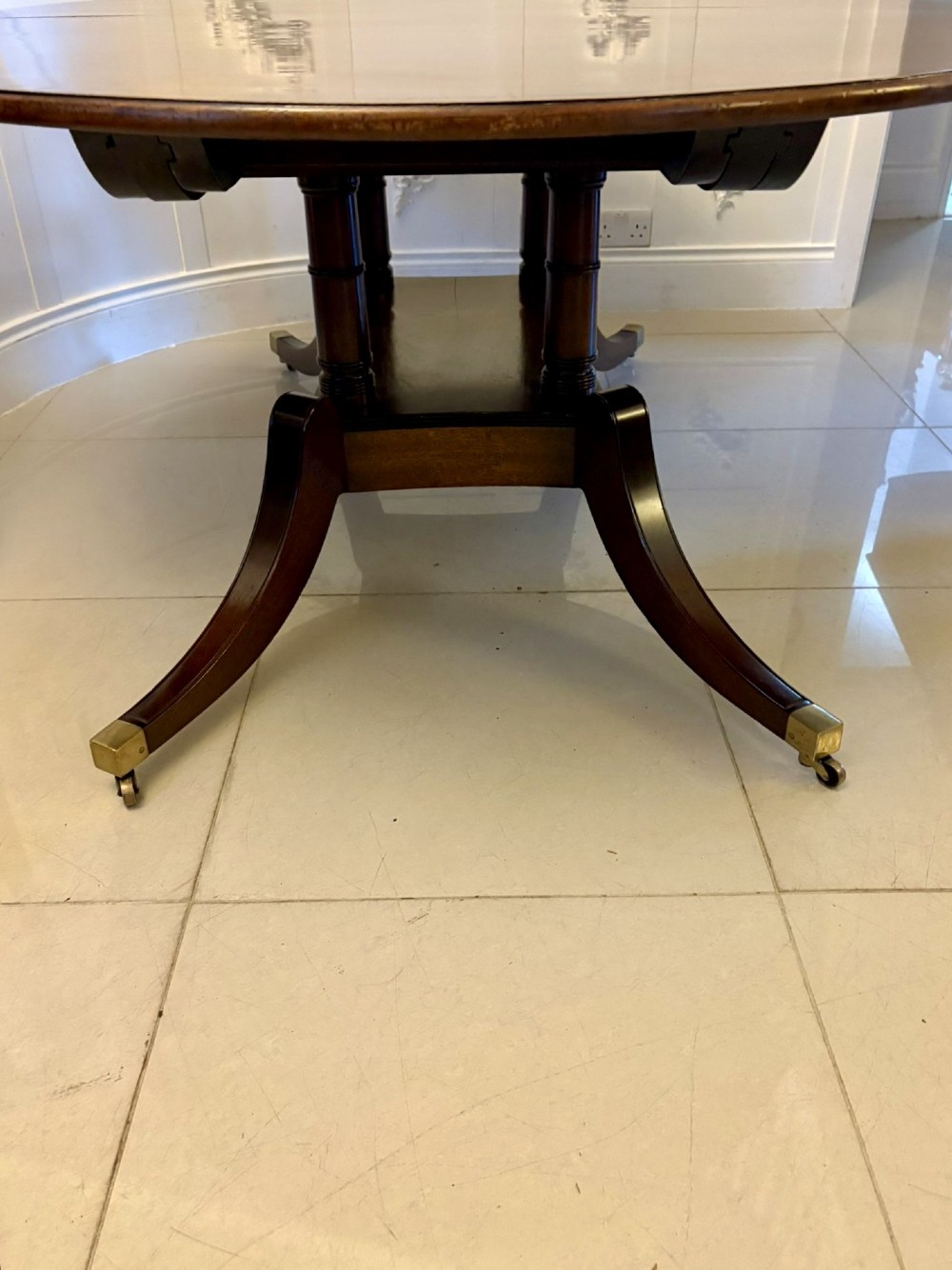 An antique oval extending mahogany dining table on splayed pedestal legs with brass castors. View XIV