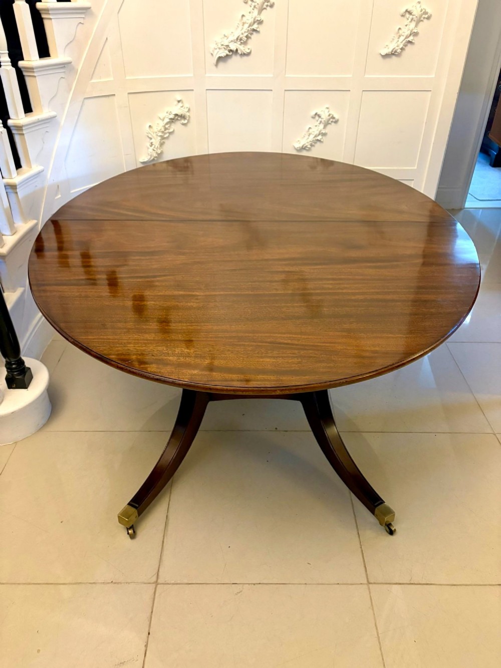 An antique oval extending mahogany dining table on splayed pedestal legs with brass castors. View XV