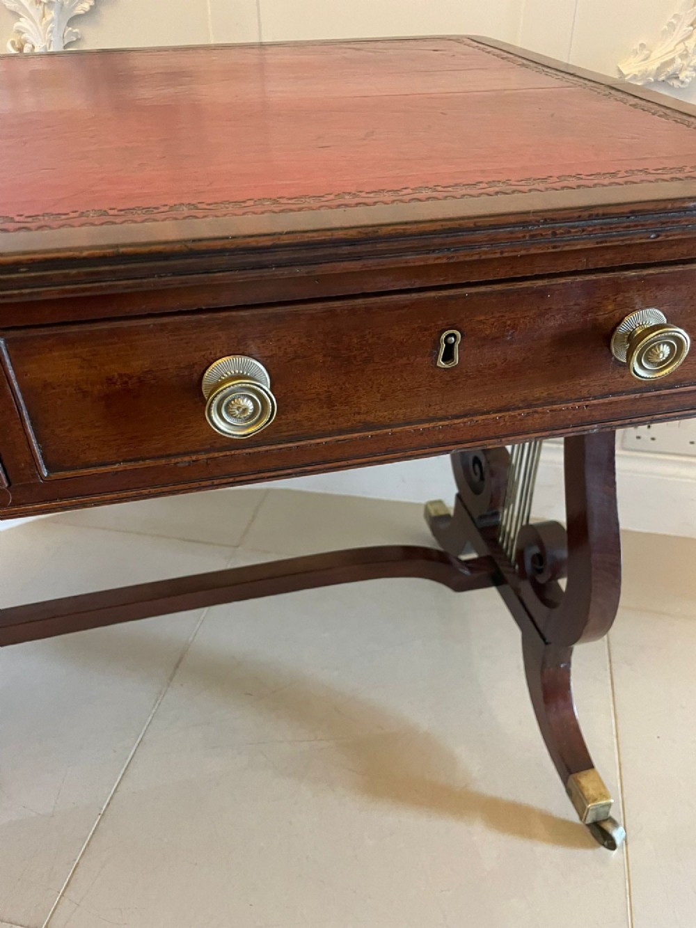 An antique Regency mahogany free-standing writing desk featuring a red leather gilt-tooled insert, two frieze drawers, lyre-form end supports, and brass castors. View V