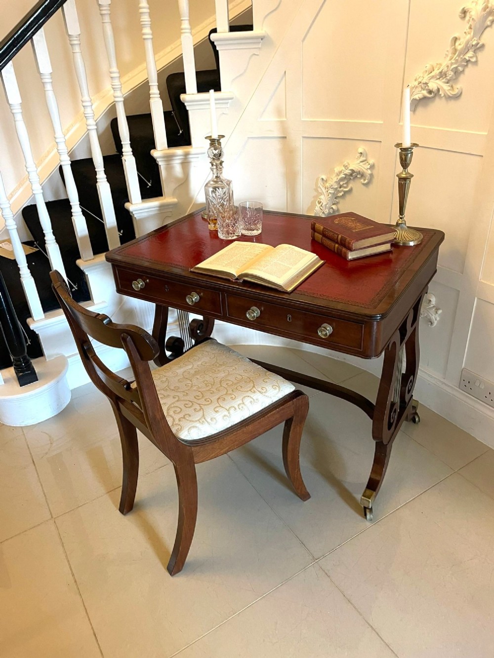 An antique Regency mahogany free-standing writing desk featuring a red leather gilt-tooled insert, two frieze drawers, lyre-form end supports, and brass castors. View VI
