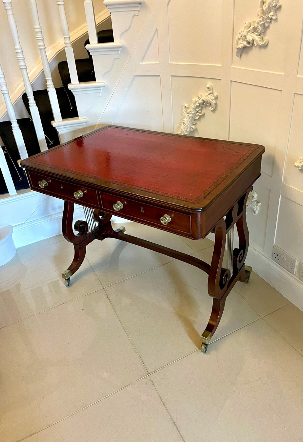 An antique Regency mahogany free-standing writing desk featuring a red leather gilt-tooled insert, two frieze drawers, lyre-form end supports, and brass castors. View VII