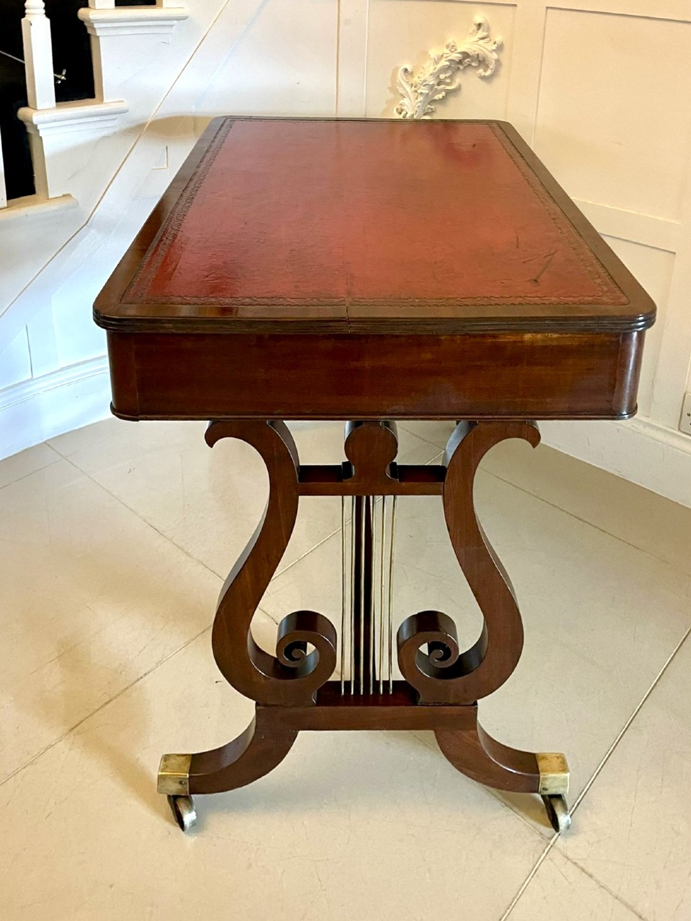 An antique Regency mahogany free-standing writing desk featuring a red leather gilt-tooled insert, two frieze drawers, lyre-form end supports, and brass castors. View VIII
