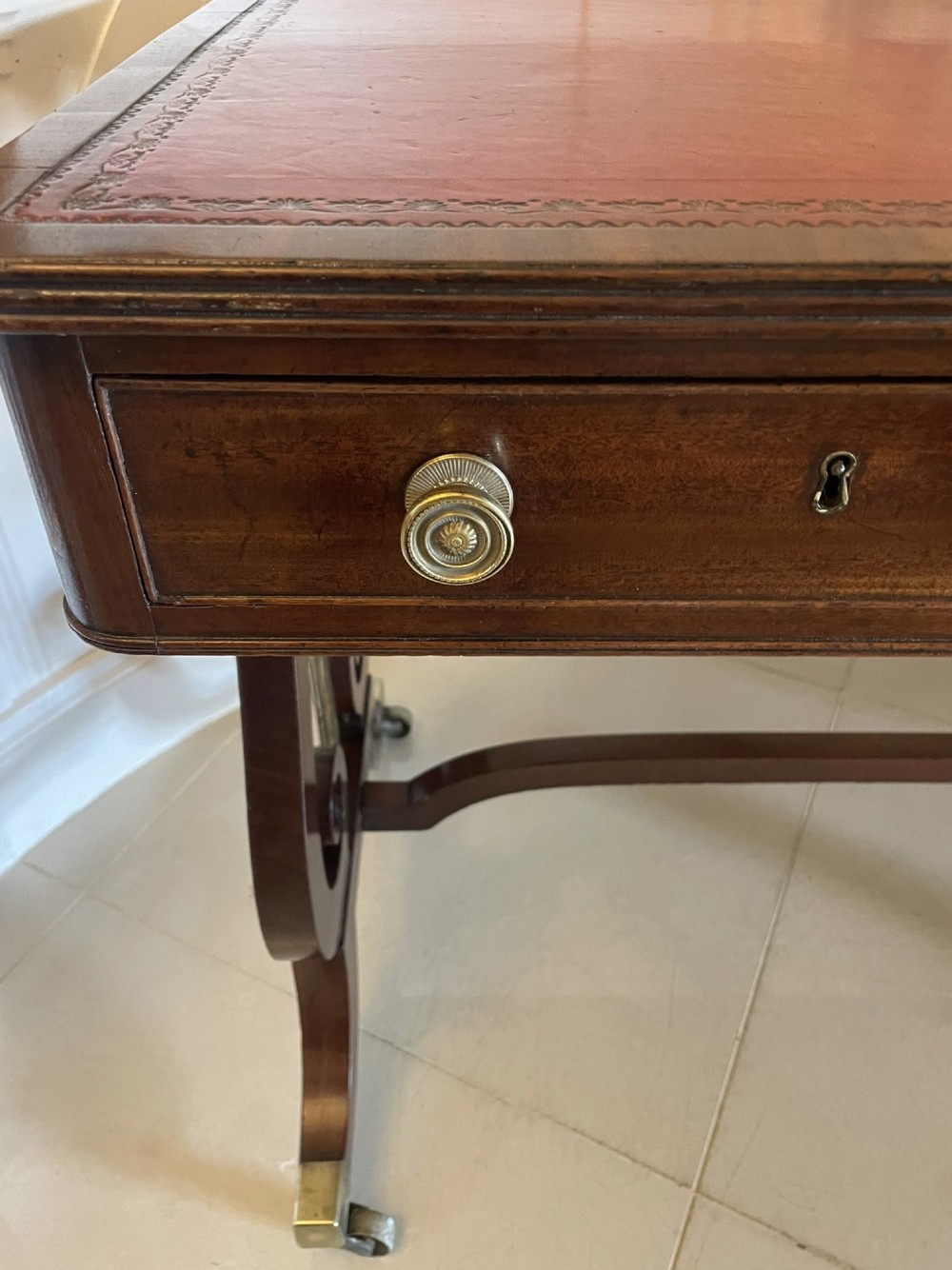An antique Regency mahogany free-standing writing desk featuring a red leather gilt-tooled insert, two frieze drawers, lyre-form end supports, and brass castors. View XII
