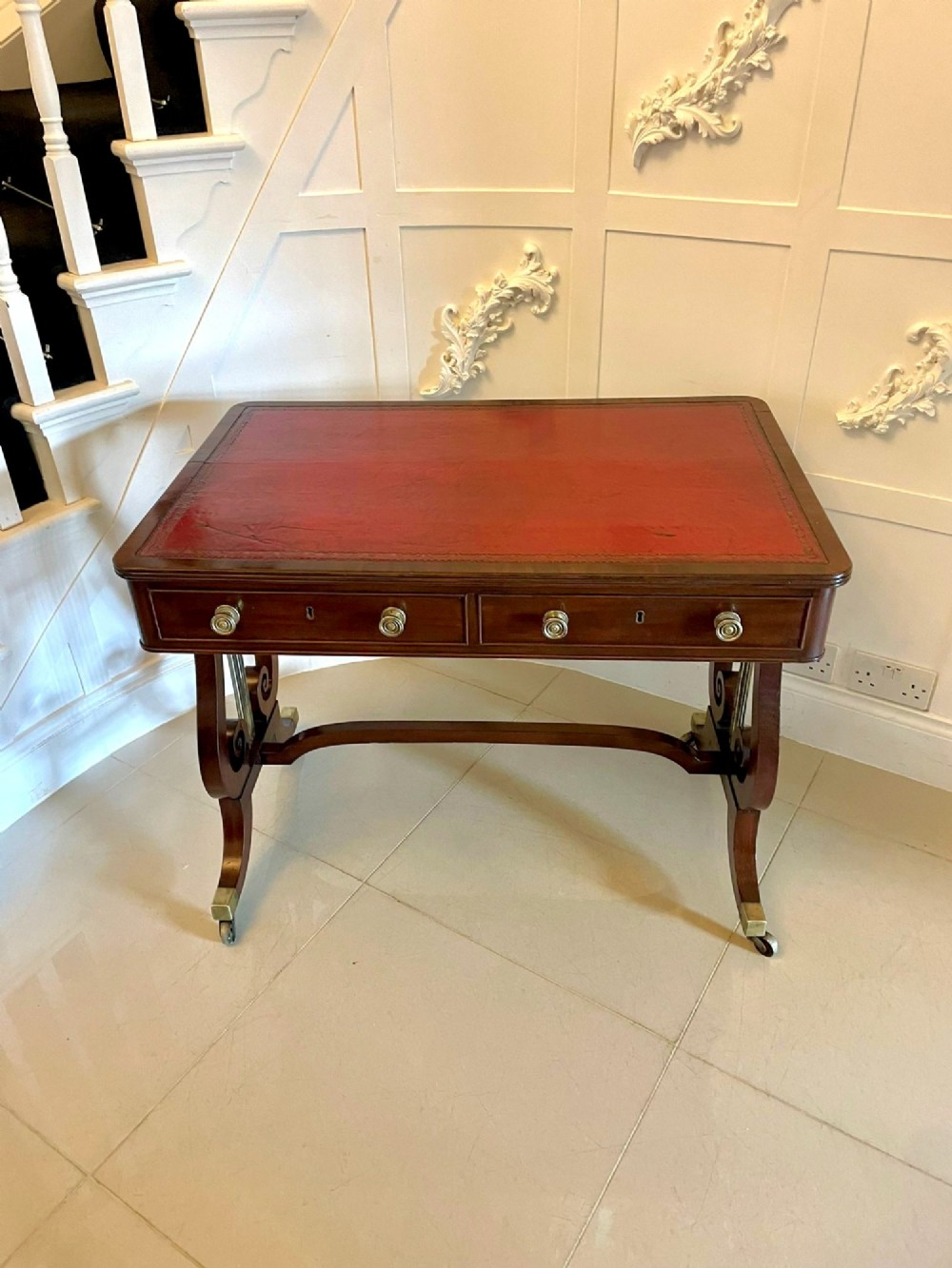 An antique Regency mahogany free-standing writing desk featuring a red leather gilt-tooled insert, two frieze drawers, lyre-form end supports, and brass castors. View XIII