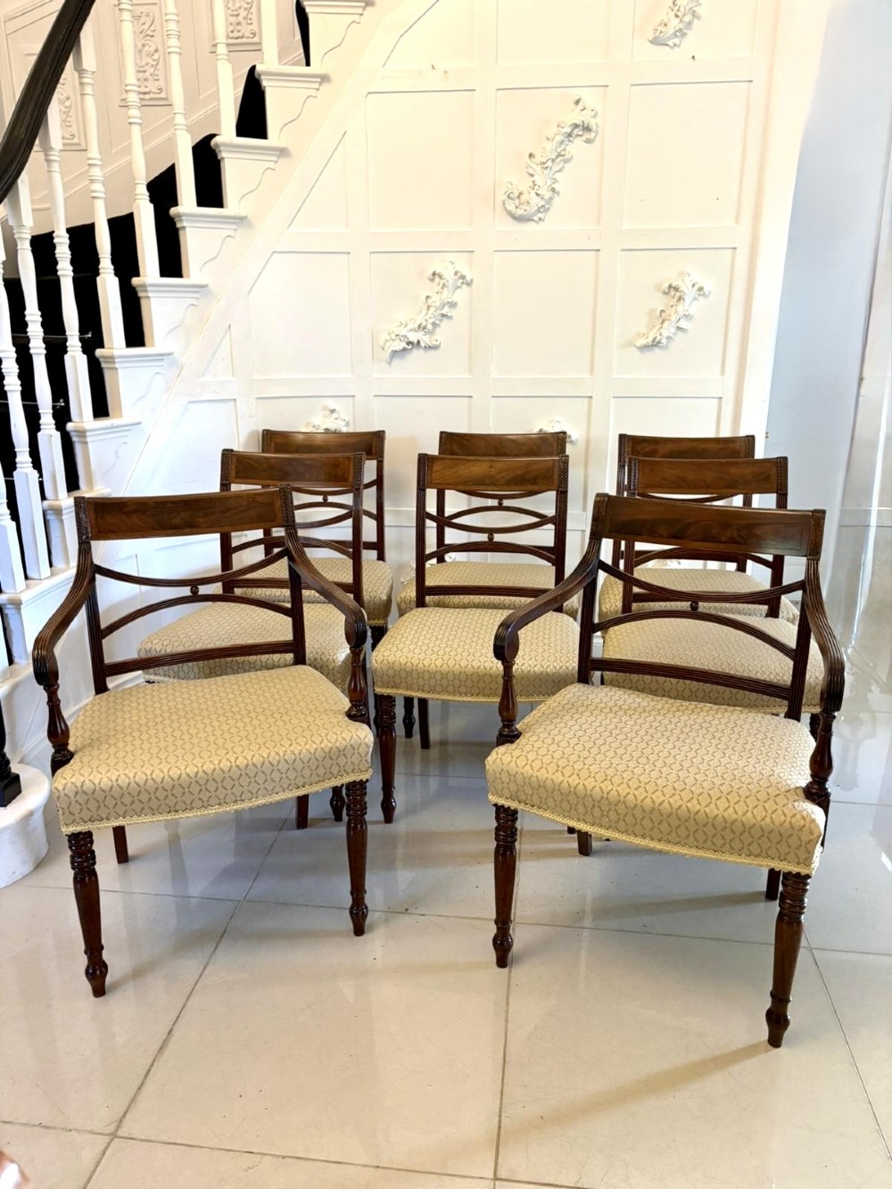 A set of eight George III style mahogany dining chairs featuring two carvers and six side chairs with reeded frames and patterned cream upholstered seats.
