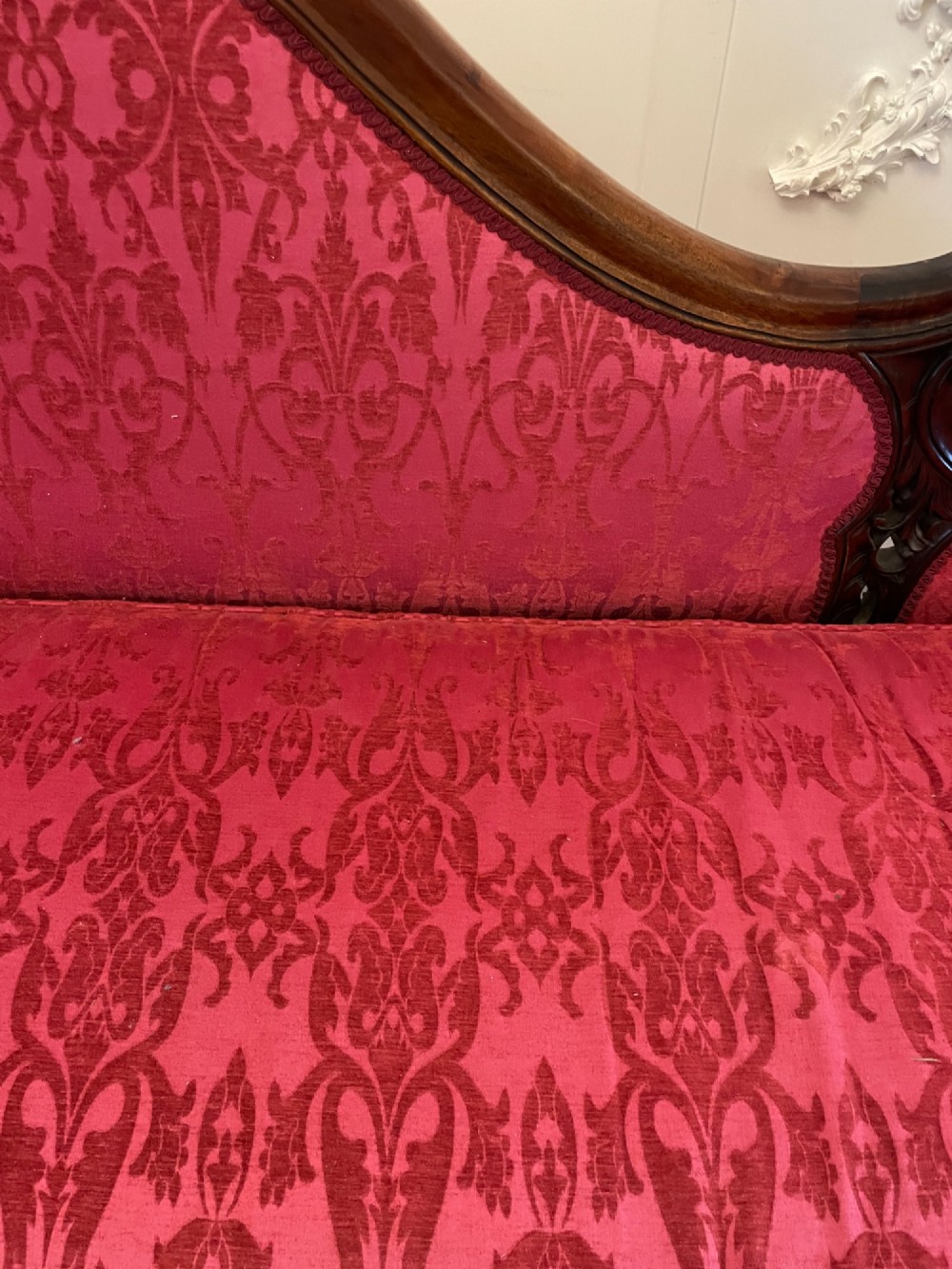 An antique Victorian carved mahogany chaise longue upholstered in deep red damask fabric with cabriole legs and ornate timber carving. View II