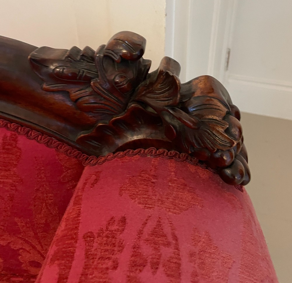 An antique Victorian carved mahogany chaise longue upholstered in deep red damask fabric with cabriole legs and ornate timber carving. View VI