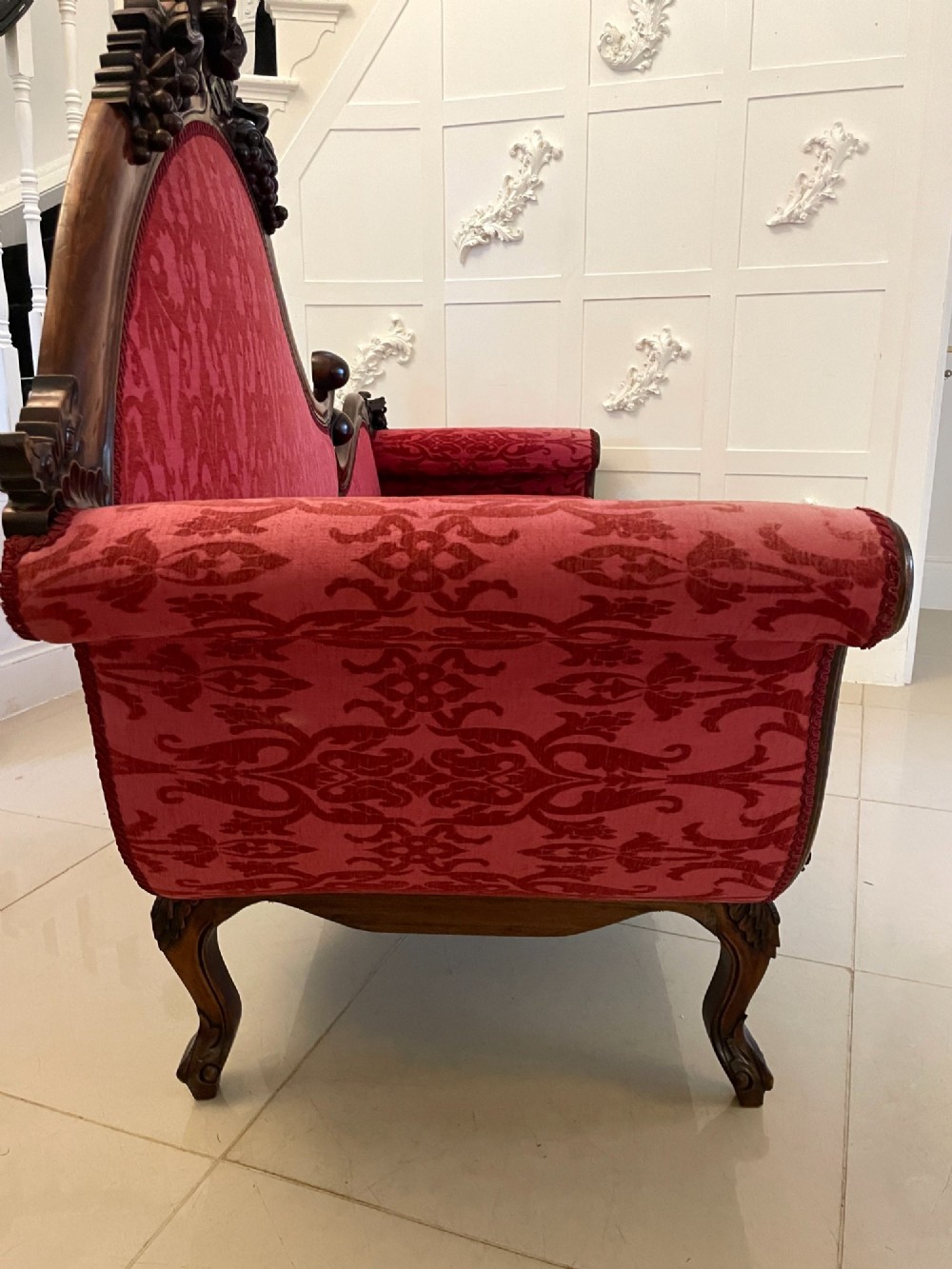 An antique Victorian carved mahogany chaise longue upholstered in deep red damask fabric with cabriole legs and ornate timber carving. View XII