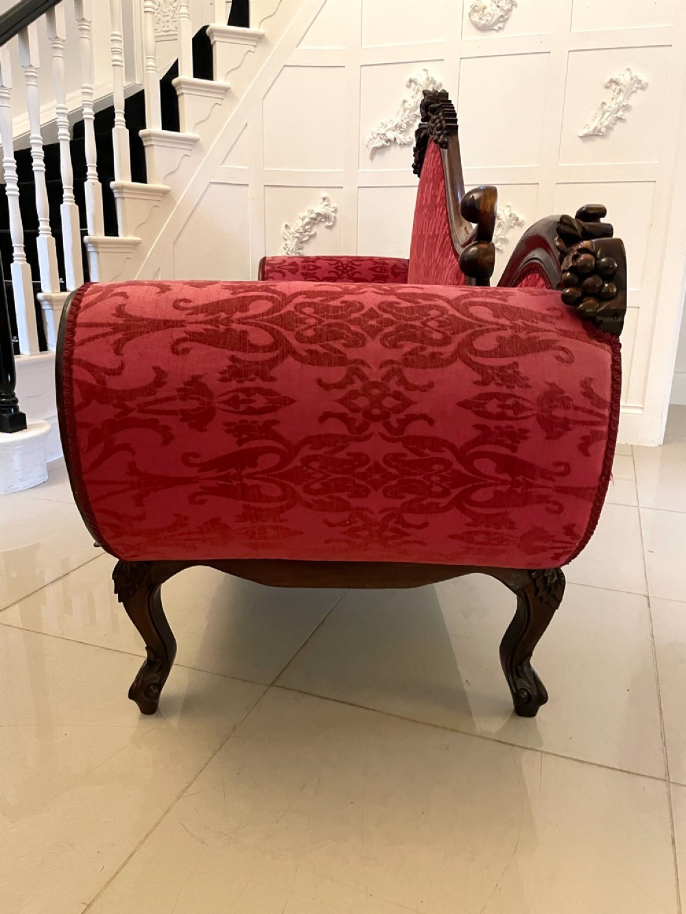 An antique Victorian carved mahogany chaise longue upholstered in deep red damask fabric with cabriole legs and ornate timber carving. View XIV