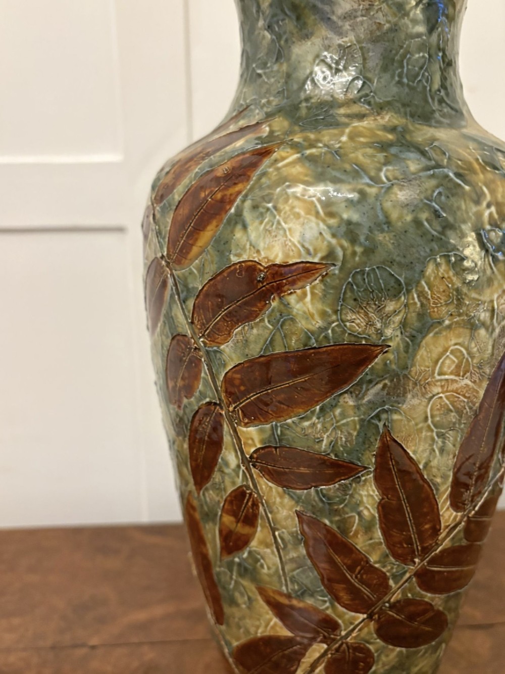 A tall Victorian glazed stoneware vase featuring a mottled green background decorated with brown leaf impressions and a flared rim. View VI