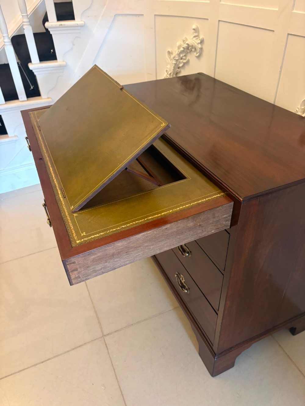A George II mahogany chest of drawers featuring an open top writing drawer with an adjustable gilt-tooled green leather surface and brass handles. View X