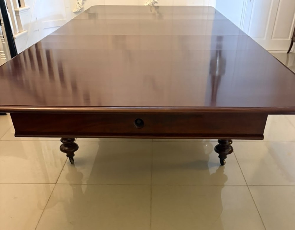 A large William IV figured mahogany extending dining table with a polished surface, rounded corners, and turned legs on brass castors. View XII