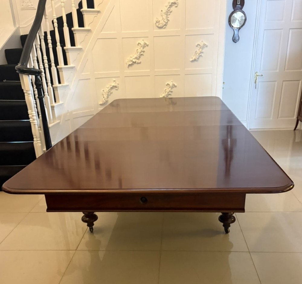 A large William IV figured mahogany extending dining table with a polished surface, rounded corners, and turned legs on brass castors.