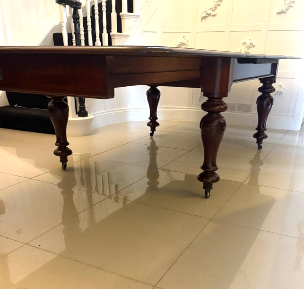 A large William IV figured mahogany extending dining table with a polished surface, rounded corners, and turned legs on brass castors. View XIII