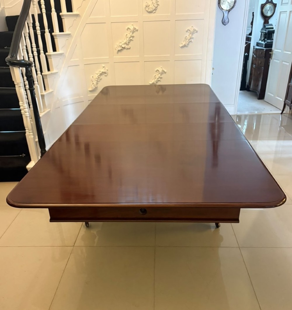 A large William IV figured mahogany extending dining table with a polished surface, rounded corners, and turned legs on brass castors. View XIV