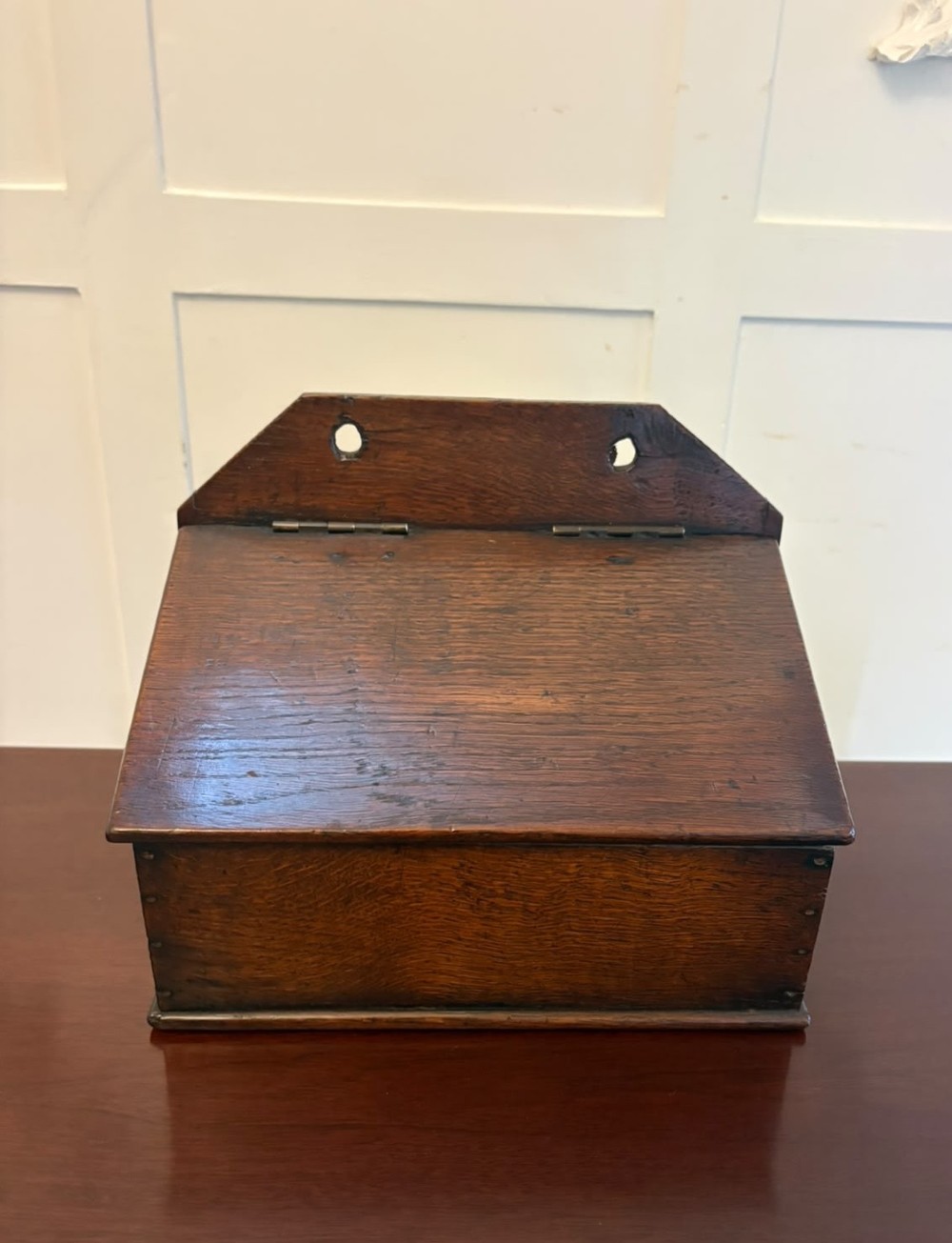 A dark oak Georgian wall-hanging candle box featuring a sloped hinged lid and a shaped backboard with two mounting holes. View VI