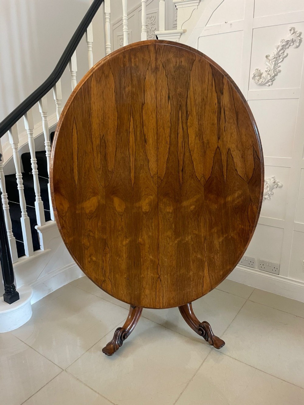 An antique Victorian rosewood tilt-top centre table shown with the circular top tilted vertically on a carved pedestal base.