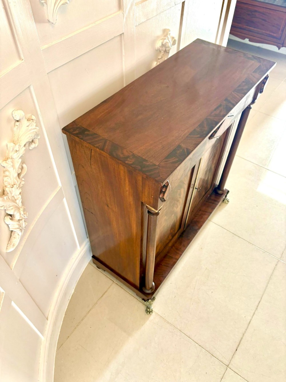 An antique Regency mahogany chiffonier cabinet featuring flame mahogany double doors, turned side columns, diamond detailing, and metal claw feet. View III