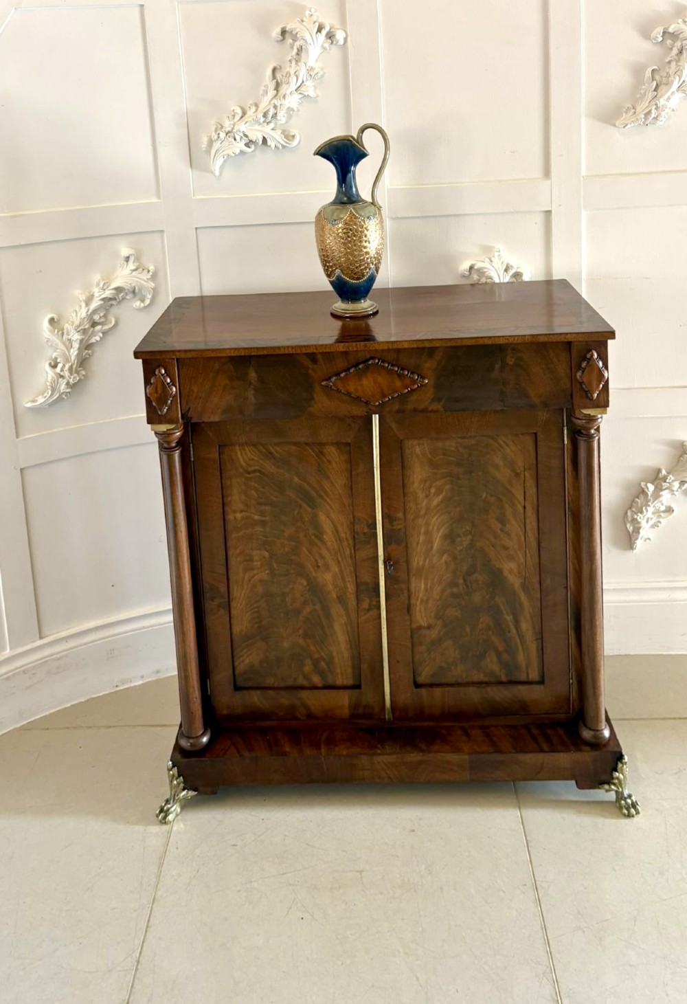 An antique Regency mahogany chiffonier cabinet featuring flame mahogany double doors, turned side columns, diamond detailing, and metal claw feet. View IV