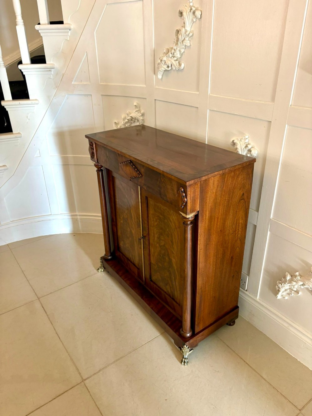 An antique Regency mahogany chiffonier cabinet featuring flame mahogany double doors, turned side columns, diamond detailing, and metal claw feet. View V