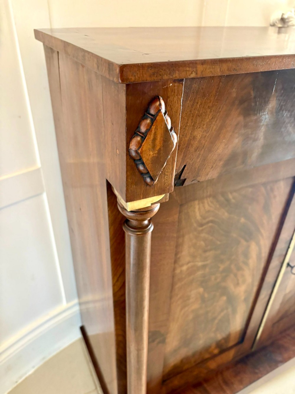 An antique Regency mahogany chiffonier cabinet featuring flame mahogany double doors, turned side columns, diamond detailing, and metal claw feet. View VI