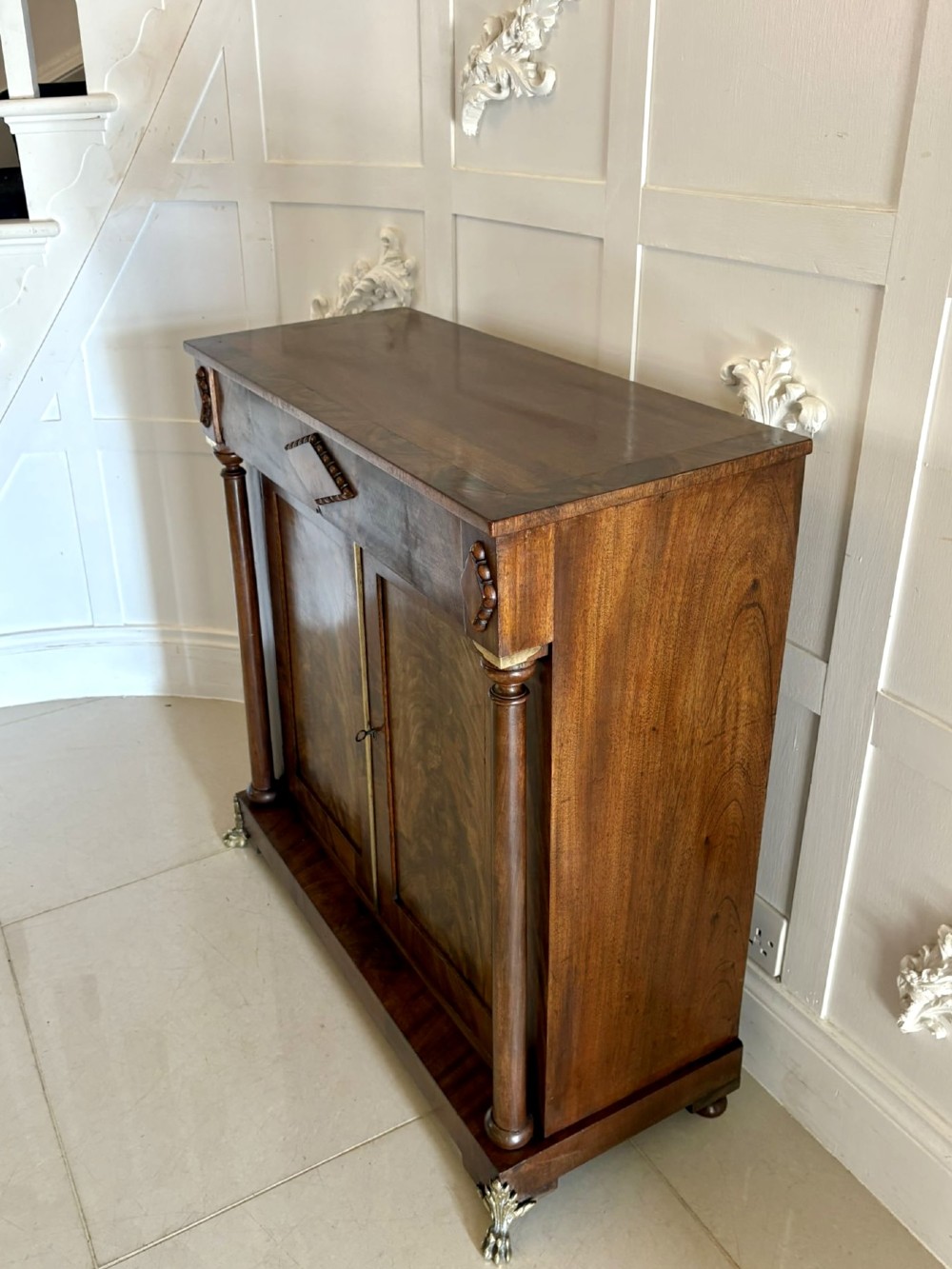 An antique Regency mahogany chiffonier cabinet featuring flame mahogany double doors, turned side columns, diamond detailing, and metal claw feet. View VIII