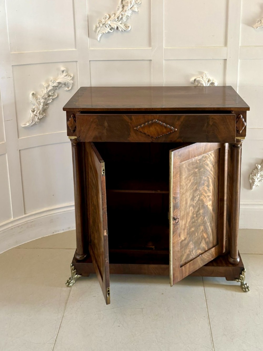 An antique Regency mahogany chiffonier cabinet featuring flame mahogany double doors, turned side columns, diamond detailing, and metal claw feet. View IX