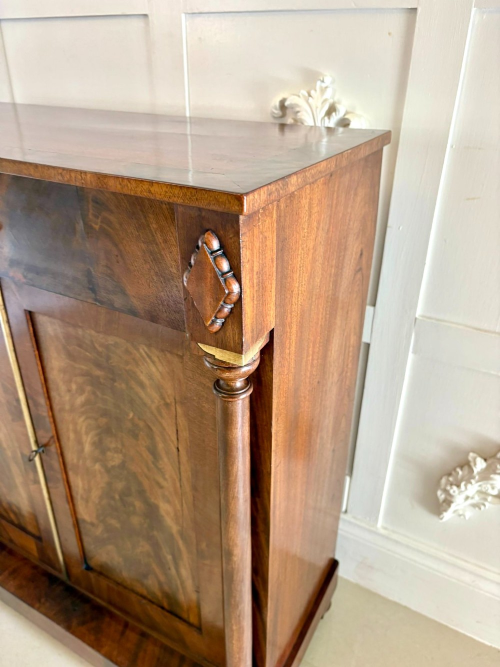 An antique Regency mahogany chiffonier cabinet featuring flame mahogany double doors, turned side columns, diamond detailing, and metal claw feet. View X