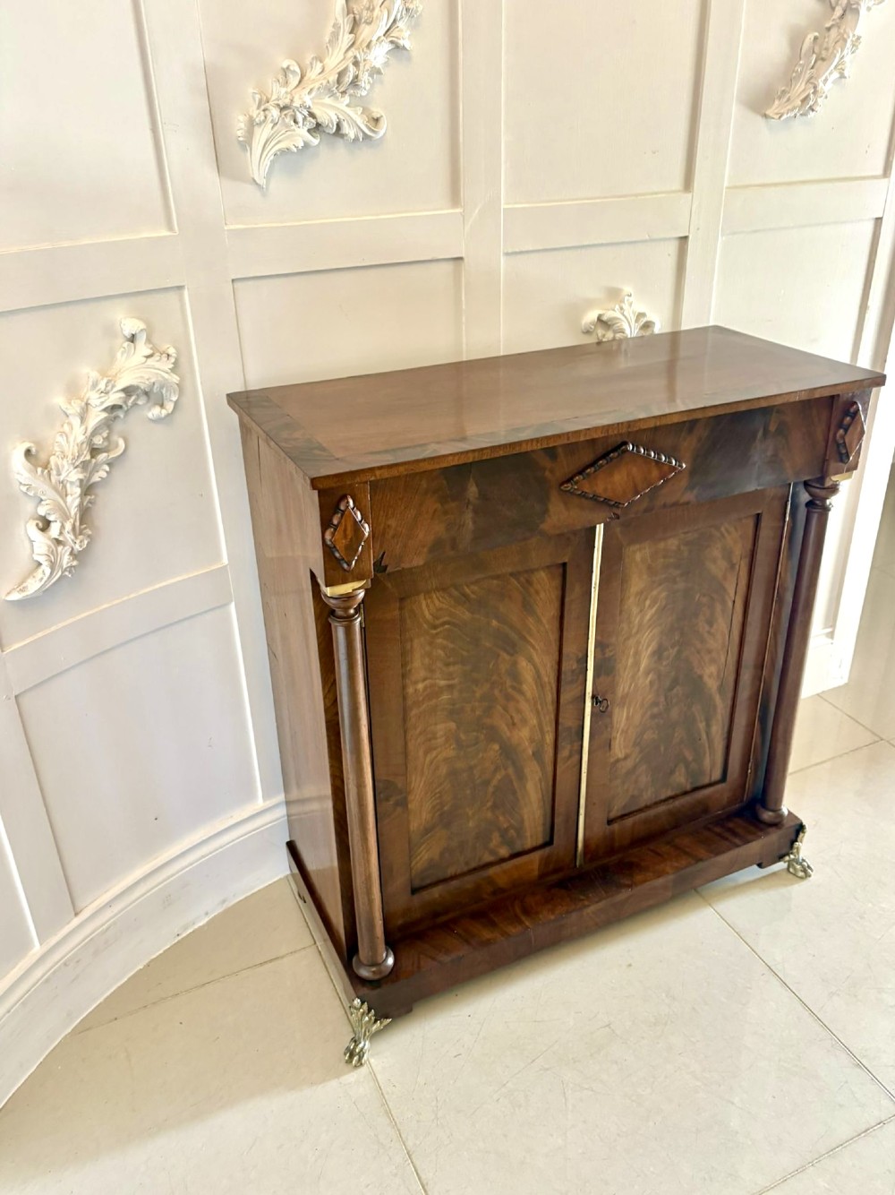 An antique Regency mahogany chiffonier cabinet featuring flame mahogany double doors, turned side columns, diamond detailing, and metal claw feet.