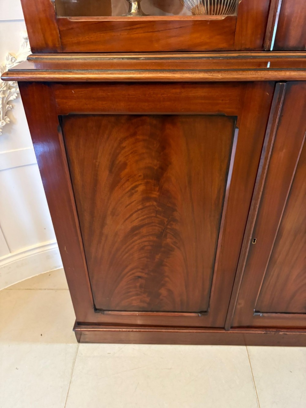 An antique Victorian mahogany bookcase featuring two upper glass-glazed doors and two lower flame mahogany panelled cupboard doors. View V