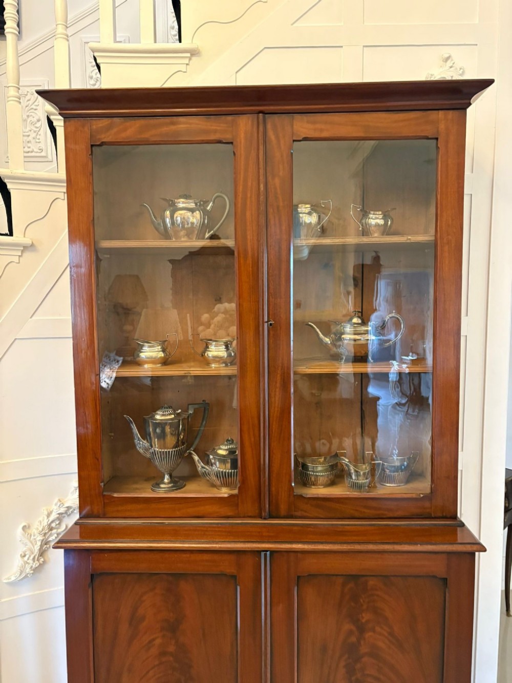 An antique Victorian mahogany bookcase featuring two upper glass-glazed doors and two lower flame mahogany panelled cupboard doors. View VIII
