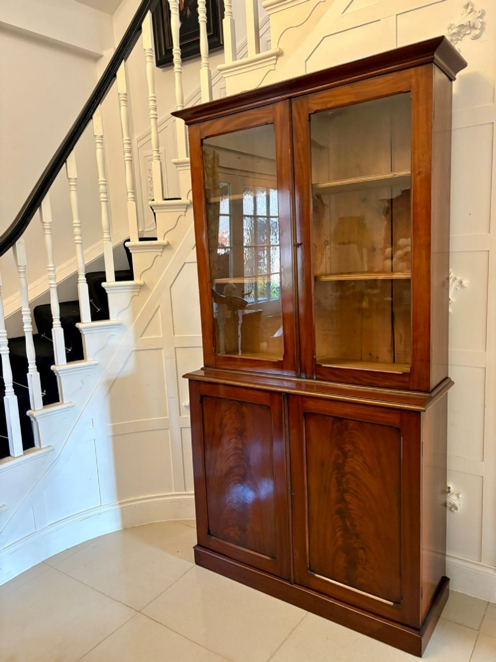 An antique Victorian mahogany bookcase featuring two upper glass-glazed doors and two lower flame mahogany panelled cupboard doors. View X