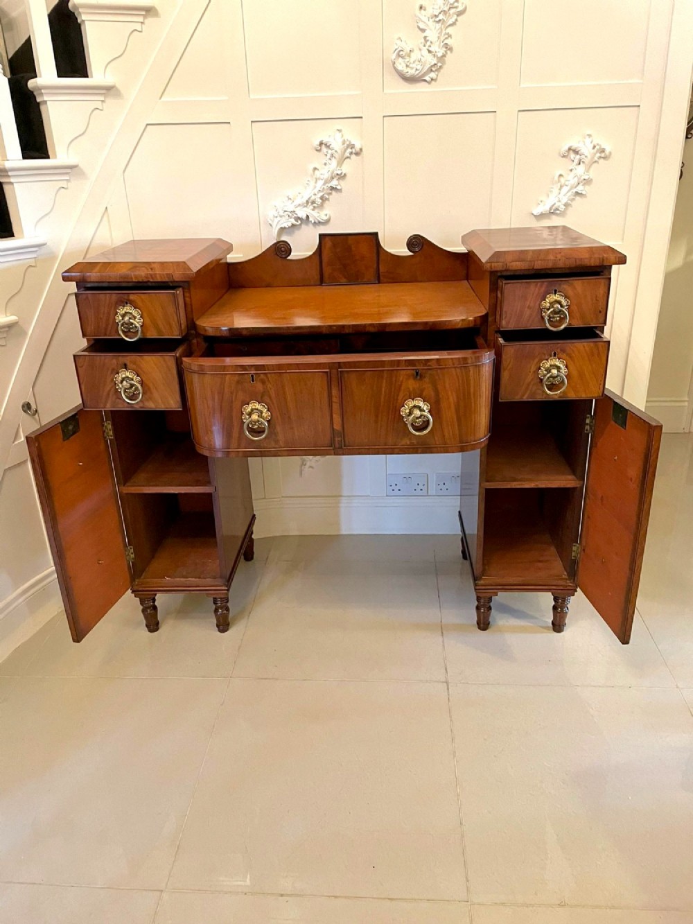 An antique Regency mahogany secretaire sideboard featuring twin pedestals, multiple drawers with brass ring pulls, and a scrolled backboard gallery. View VIII