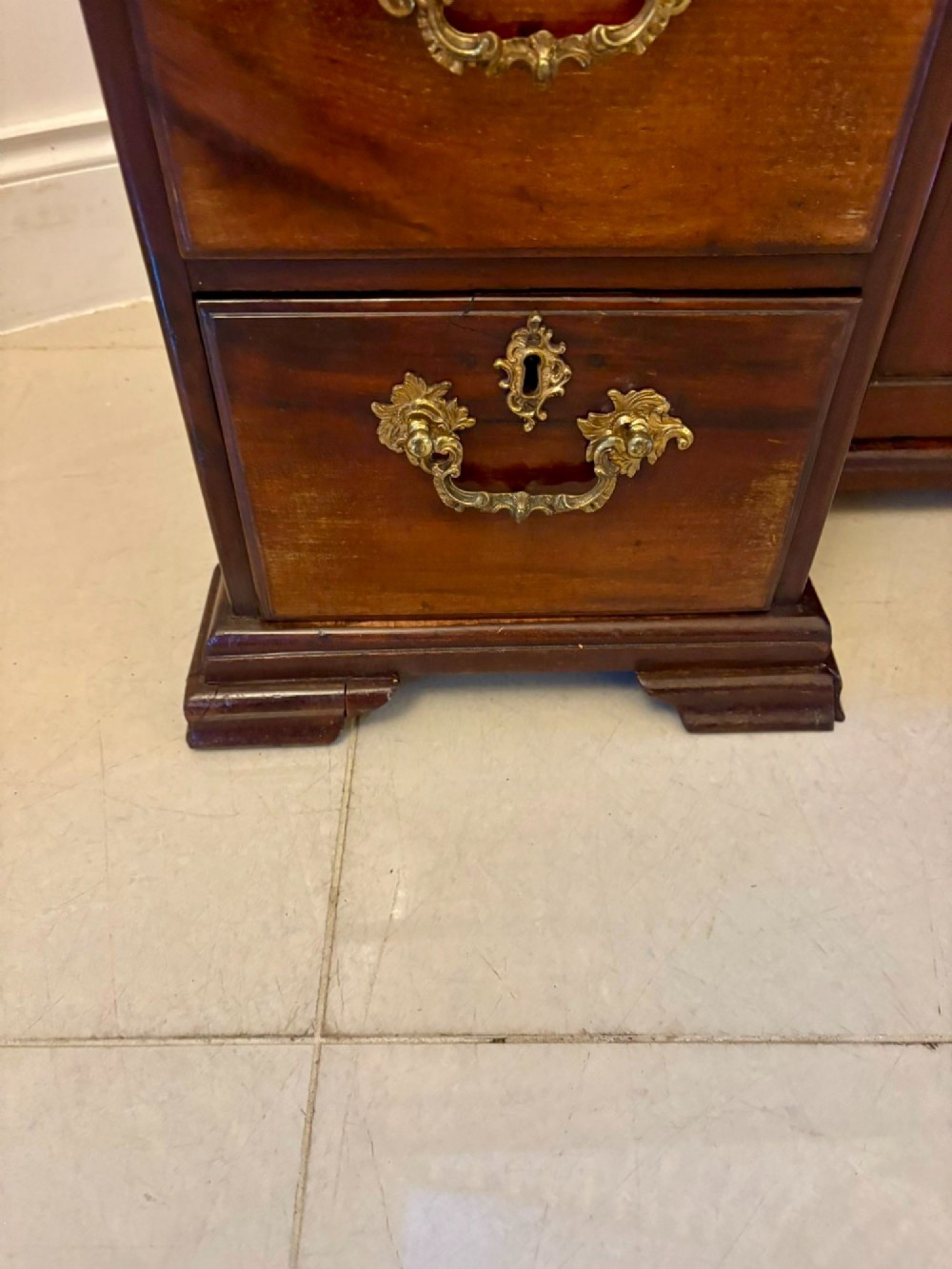 An antique George III mahogany kneehole desk featuring a green leather inset top, brass handles, a central recessed cupboard, and multiple drawers set on bracket feet. View VII