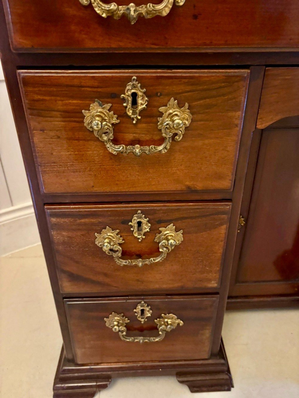 An antique George III mahogany kneehole desk featuring a green leather inset top, brass handles, a central recessed cupboard, and multiple drawers set on bracket feet. View VIII