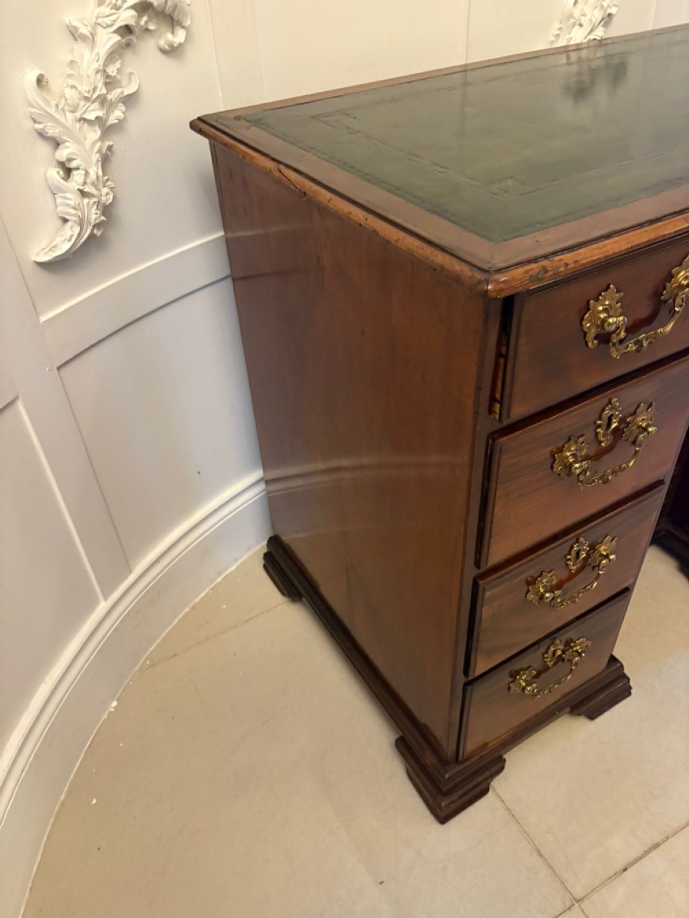 An antique George III mahogany kneehole desk featuring a green leather inset top, brass handles, a central recessed cupboard, and multiple drawers set on bracket feet. View IX