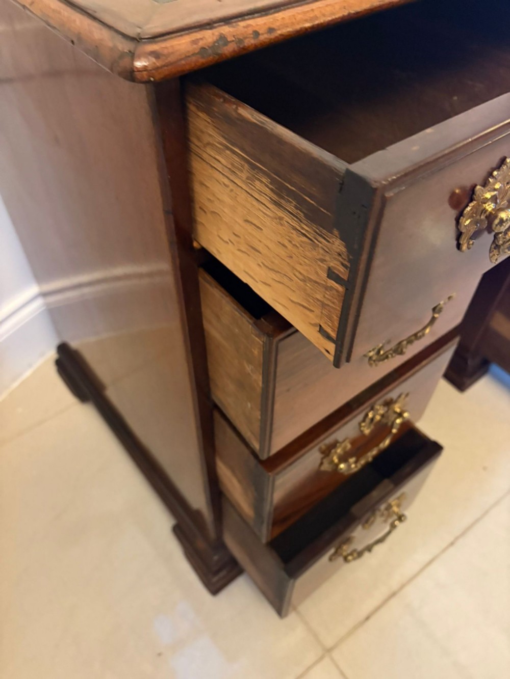 An antique George III mahogany kneehole desk featuring a green leather inset top, brass handles, a central recessed cupboard, and multiple drawers set on bracket feet. View X