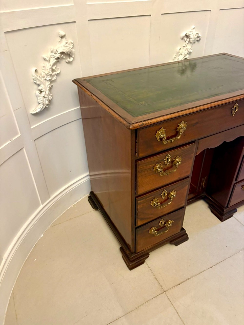An antique George III mahogany kneehole desk featuring a green leather inset top, brass handles, a central recessed cupboard, and multiple drawers set on bracket feet. View XII