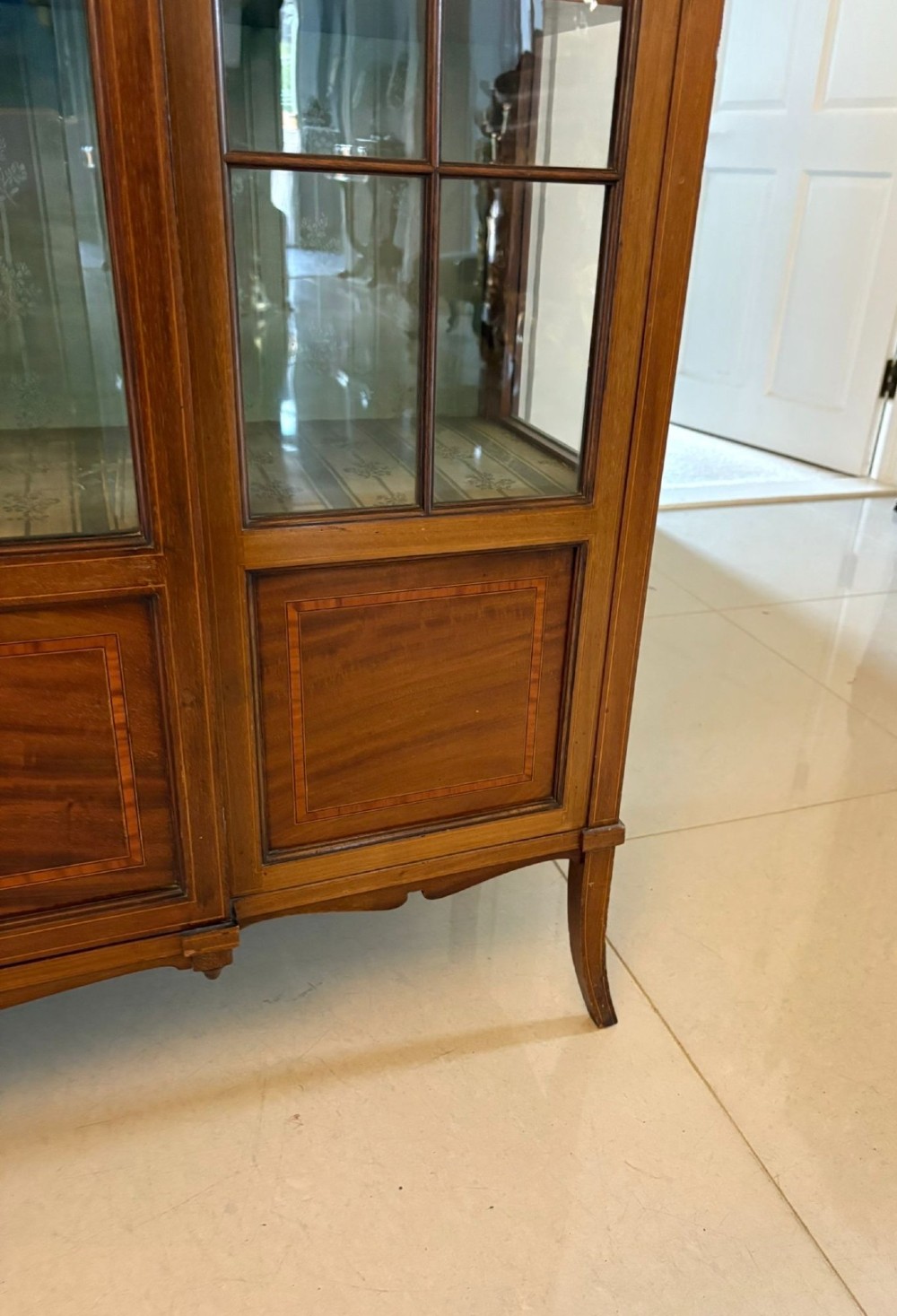 An Edwardian inlaid mahogany display cabinet featuring three glazed doors with decorative glazing bars and a fabric-lined interior. View V
