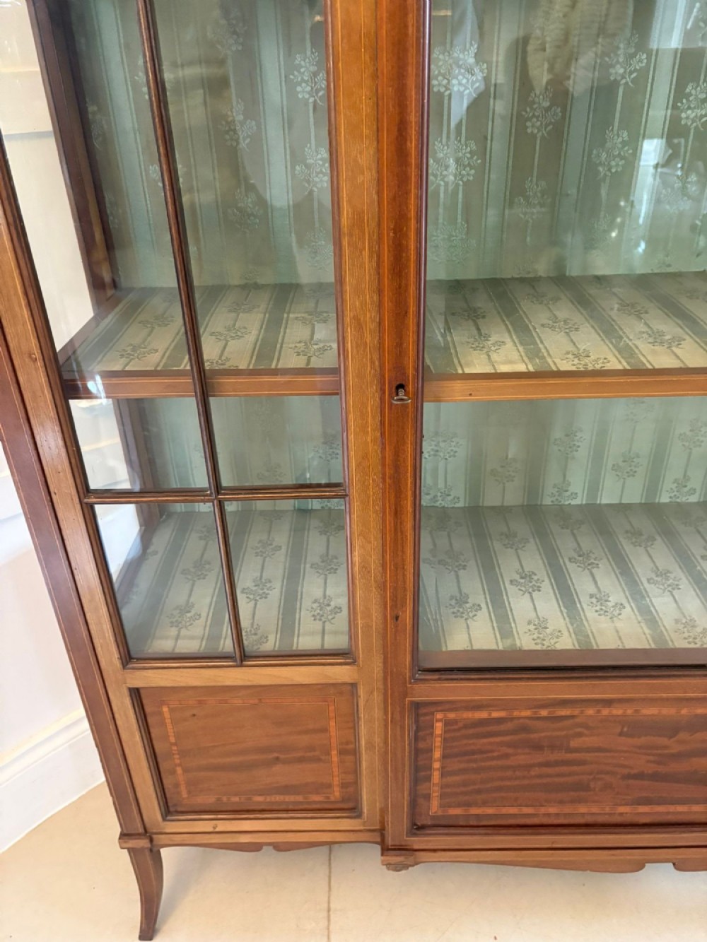 An Edwardian inlaid mahogany display cabinet featuring three glazed doors with decorative glazing bars and a fabric-lined interior. View VI