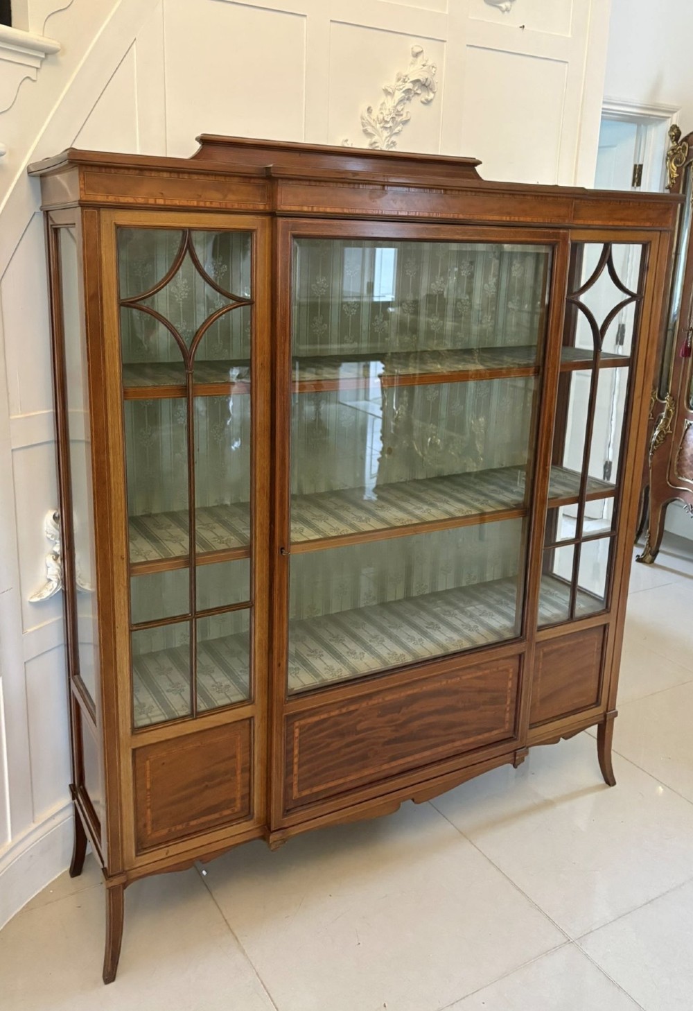 An Edwardian inlaid mahogany display cabinet featuring three glazed doors with decorative glazing bars and a fabric-lined interior. View X