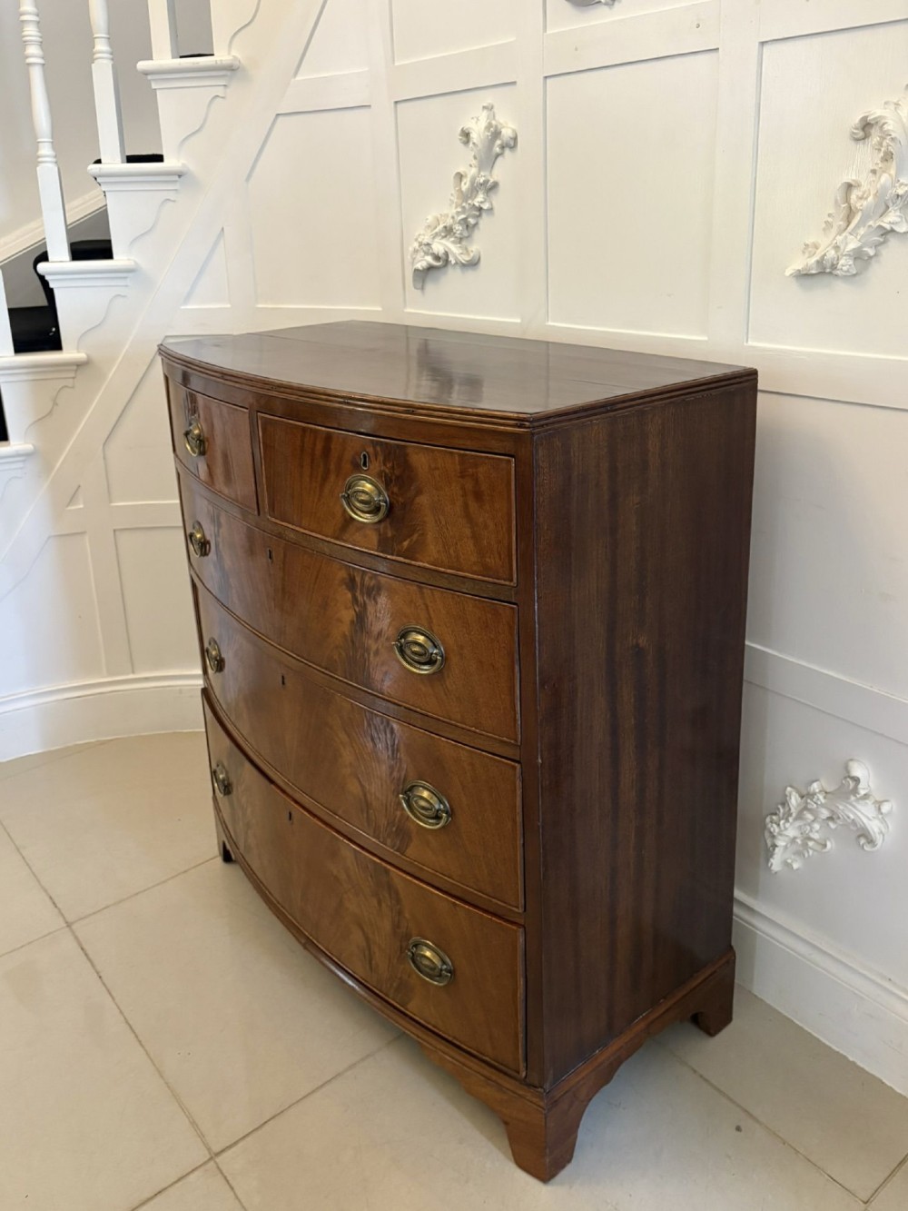 A George III mahogany bowfront chest of drawers featuring two short drawers over three long drawers with oval brass handles and splayed bracket feet. View III